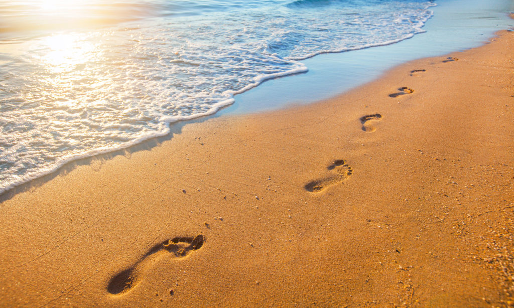 Fußabdrücke im Sandstrand am Meer als Symbol für Seebestattungen